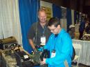  
High school student Nicholas Wattendorf, N1NRW (R), of Rhode Island hefts the PRC-150 military backpack radio — 9 pounds without battery — used by Army MARS in a demonstration of ALE at the ARRL National Centennial Convention. A new commercial transceiver at the end of the table just received his call. MARS Program Officer Paul English, WD8DBY, explains features of the PRC-150. [Matthew Hackman photo].

 